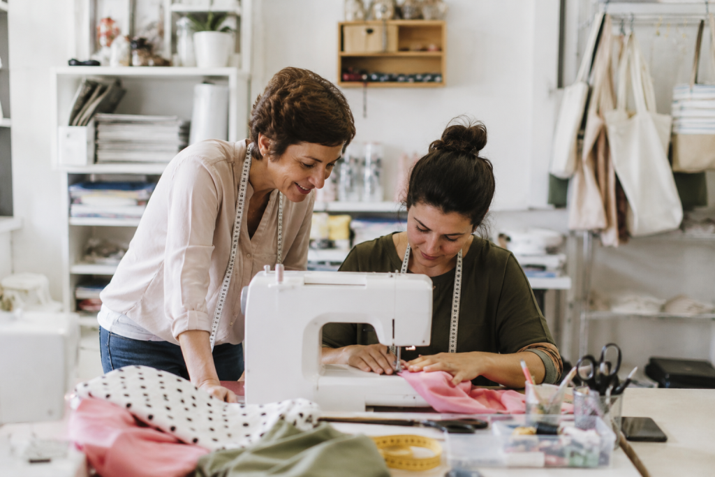 Dos personas aprenden y comparten técnicas de costura en un taller creativo. Una imagen que representa la formación práctica, el aprendizaje y la transmisión del oficio a través de la costura.
